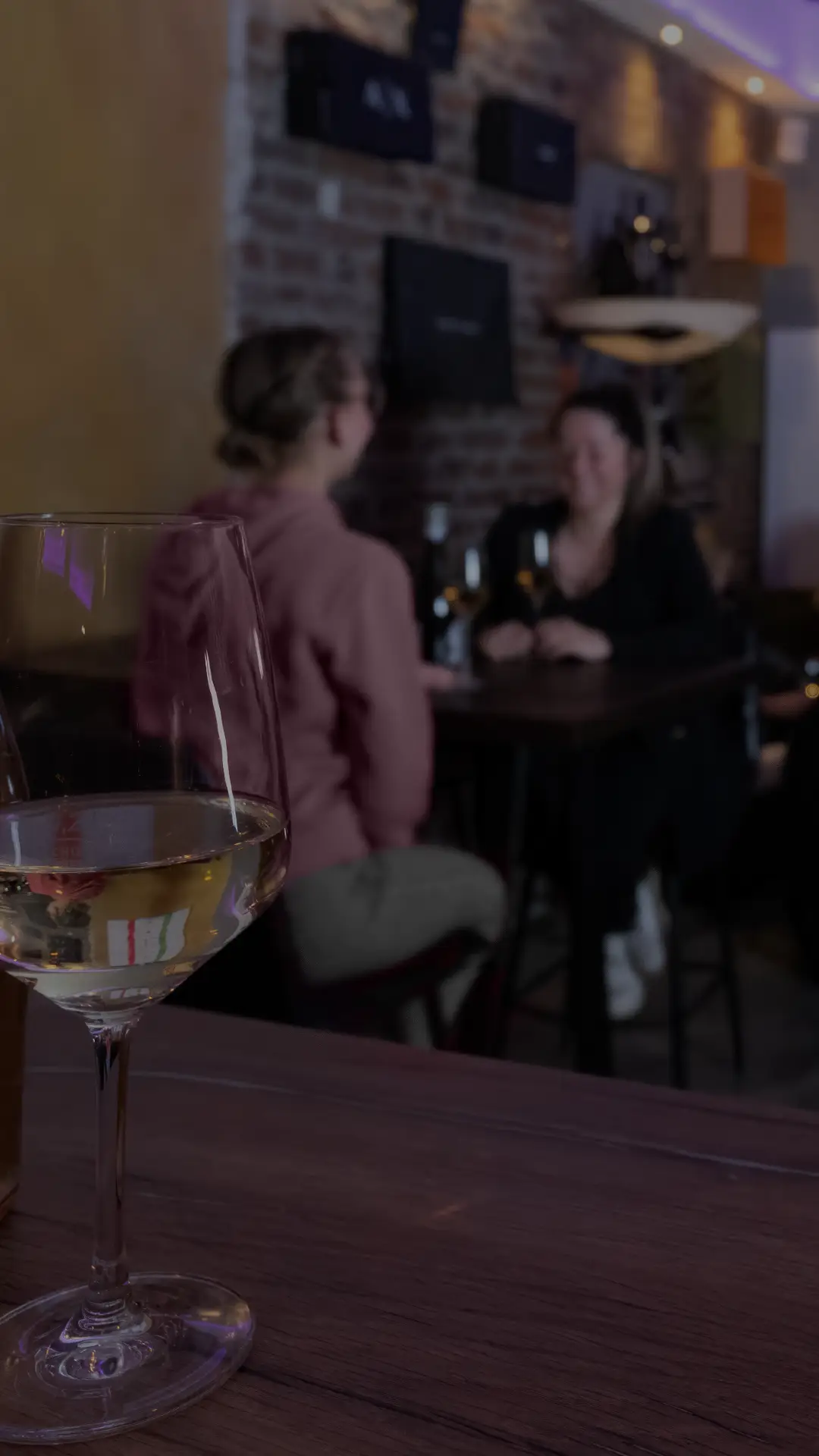 Weinglas im Vordergrund, dahinter Gäste in der Weinstube