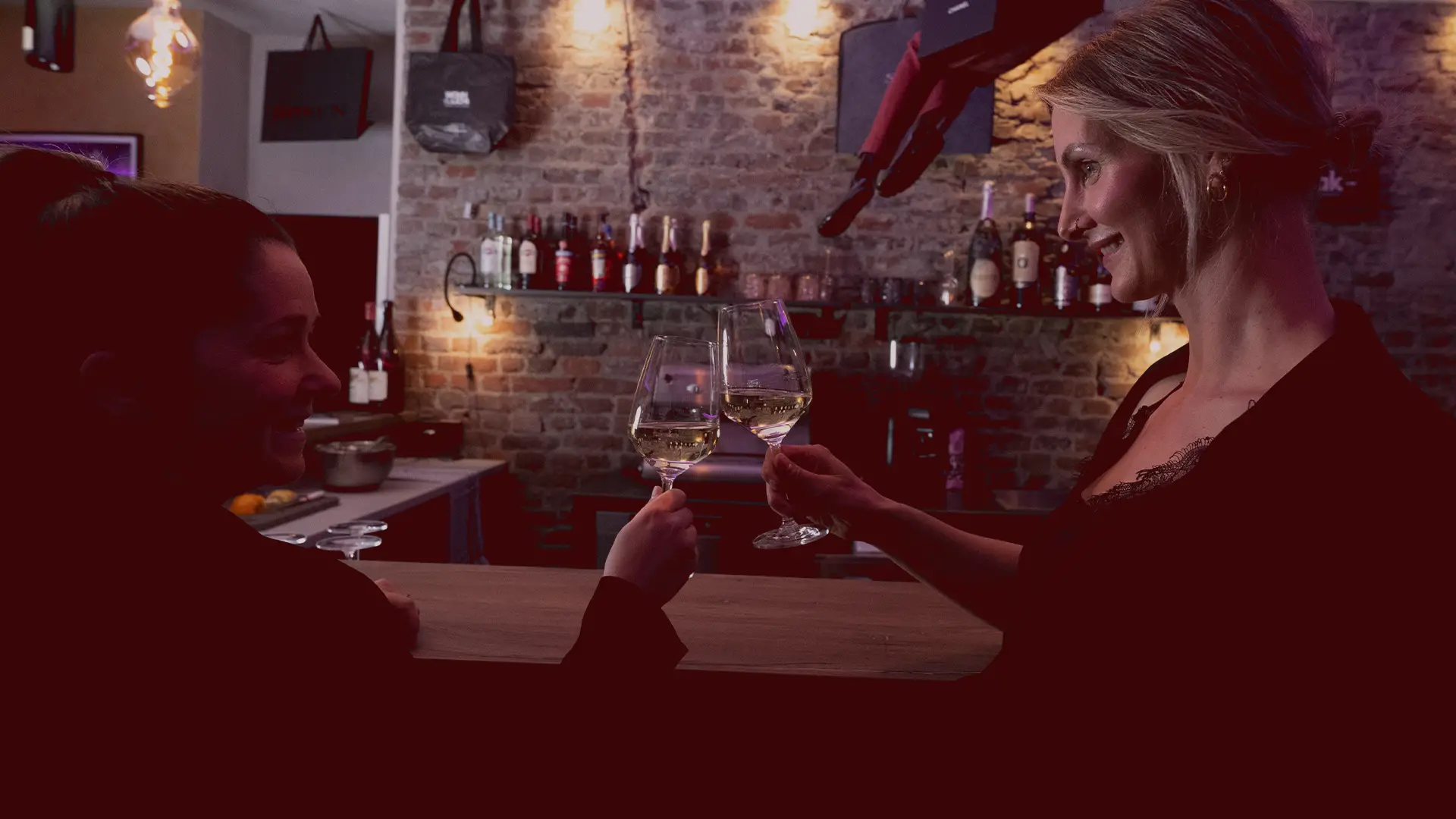 Zwei Frauen stoßen an der Theke mit Weingläsern an